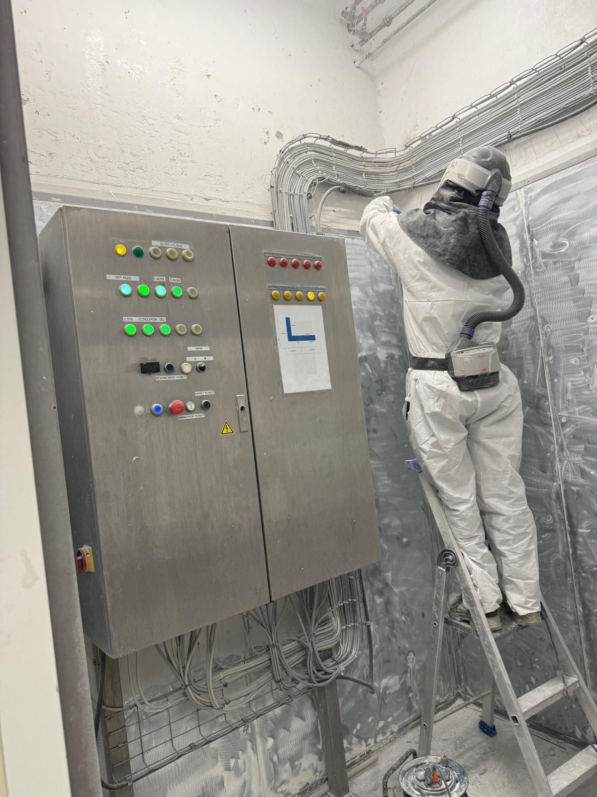 employé de la SOBRA est en plein ponçage, bien équipé avec tous les EPI nécessaires : protection respiratoire, lunettes, gants...